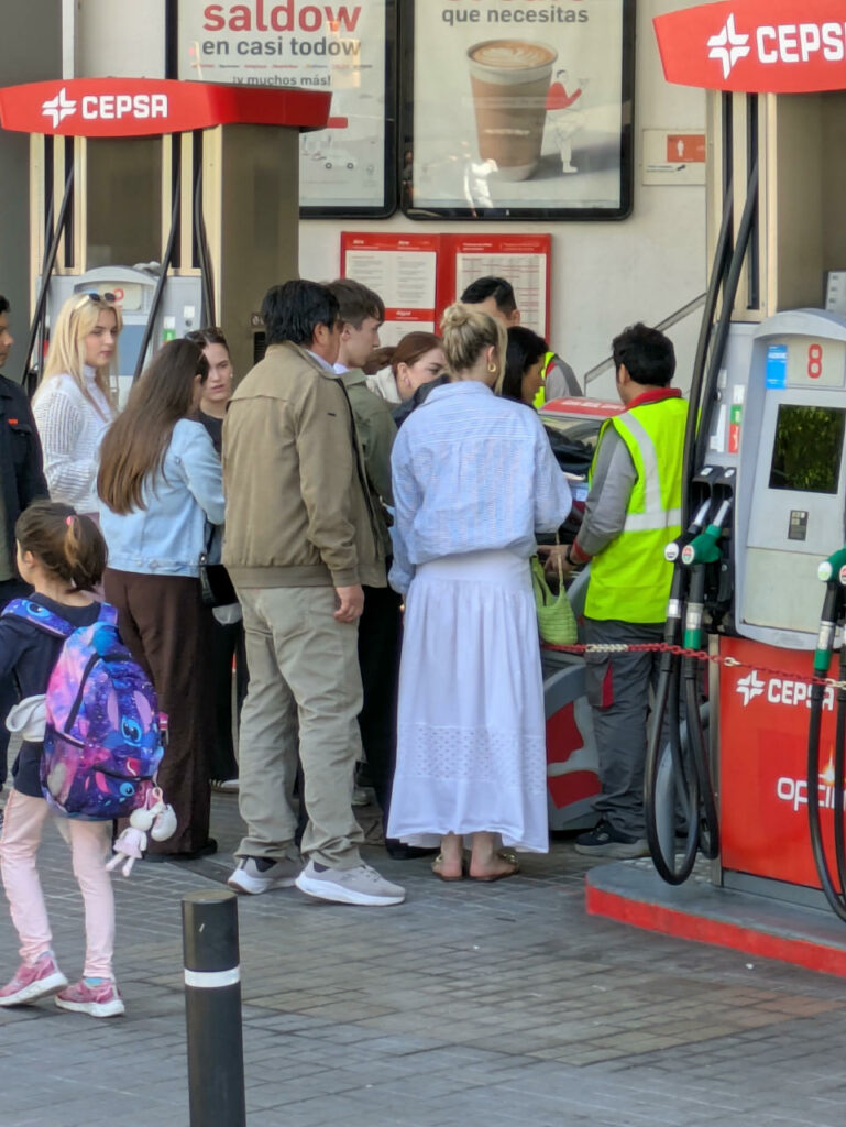 A group of people standing in the middle of a gas station.